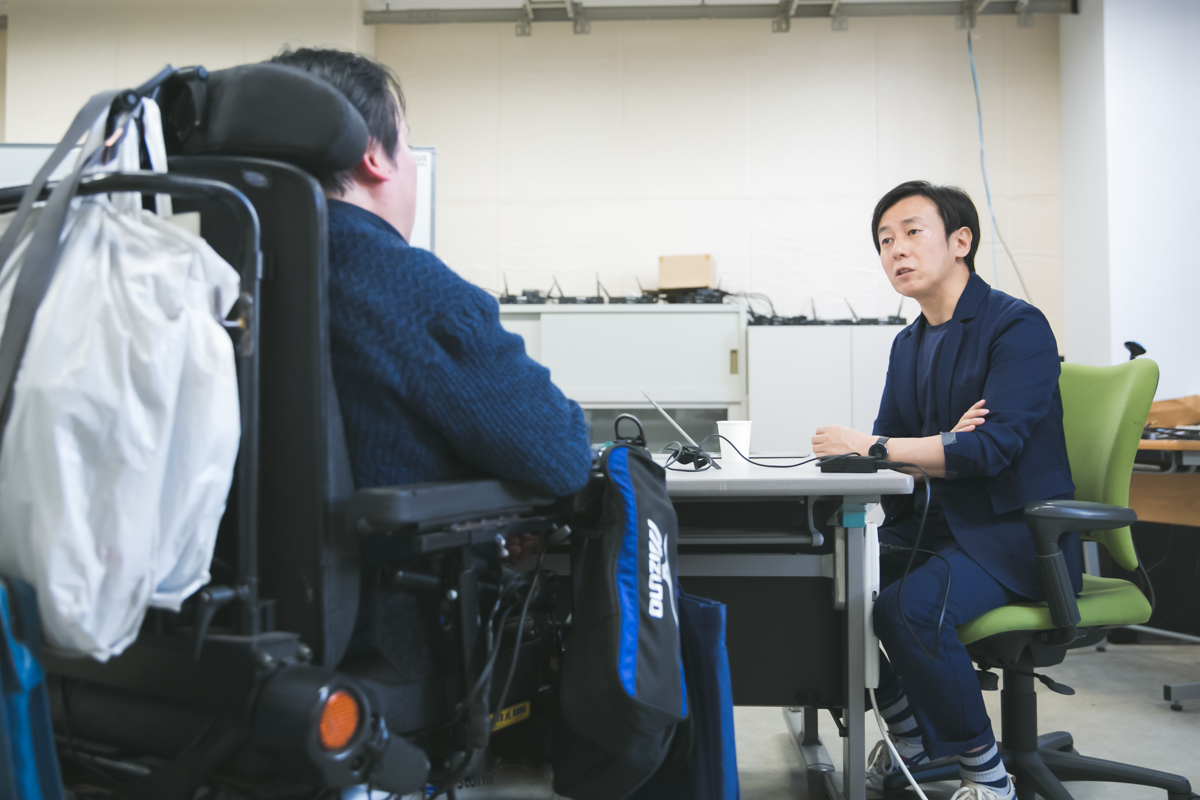 Shot of Shinichiro's wheelchair with Yoshihisa listening attentively