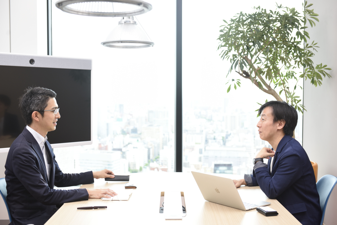 Souta Kimura and Yoshihisa Aono sitting across from each other as Yoshihisa explains something