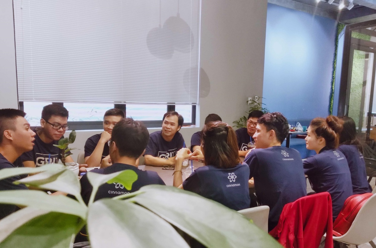 A dozen Cinnamon employees from the Vietnam office sitting around a table wearing t-shirts that say Grit